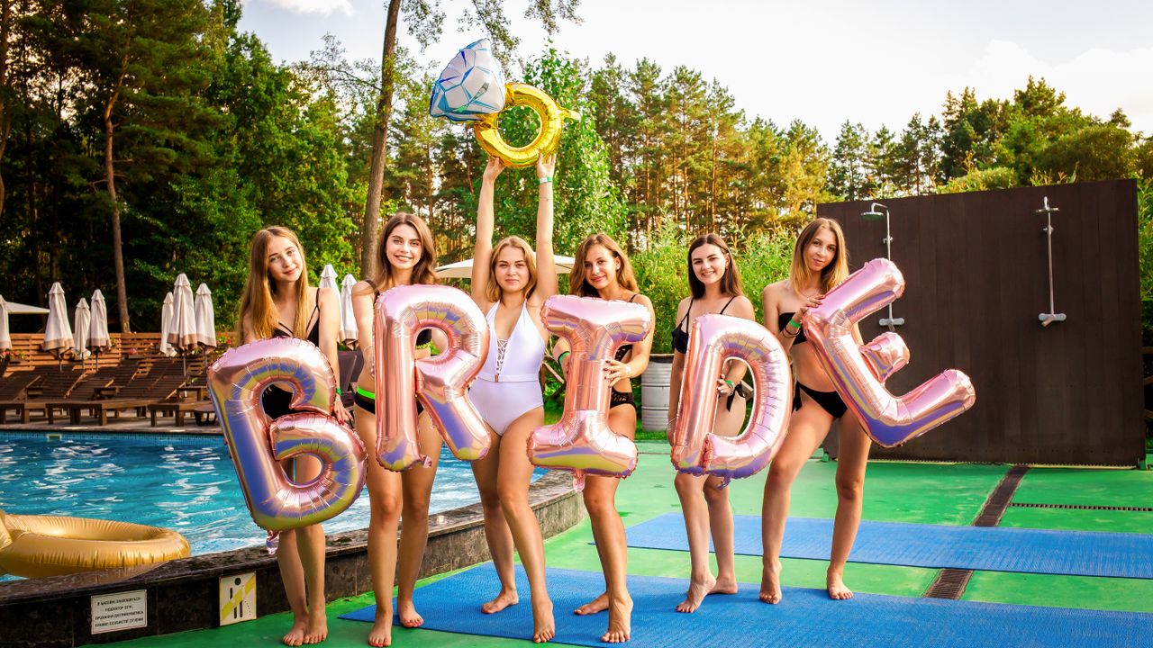 Groupe d'amies célébrant un EVJF avec des ballons BRIDE au bord d'une piscine